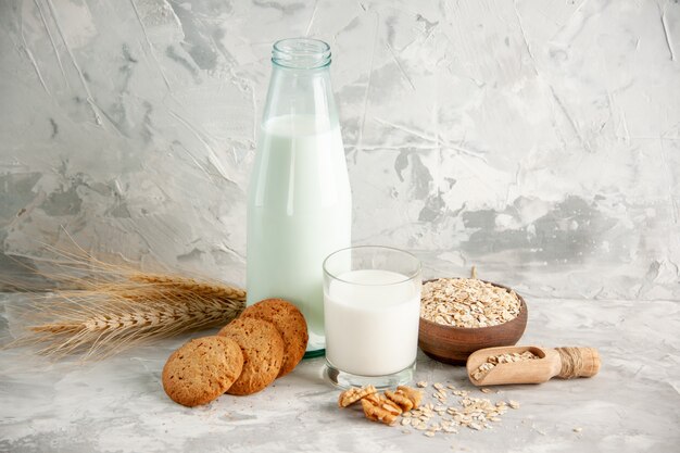 Vista superior de la botella de vidrio y taza llena de leche en bandeja de madera y galletas cuchara avena en olla marrón sobre mesa blanca sobre fondo de hielo