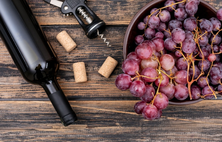 Foto gratuito vista superior botella de vino con uva en un tazón en horizontal de madera oscura
