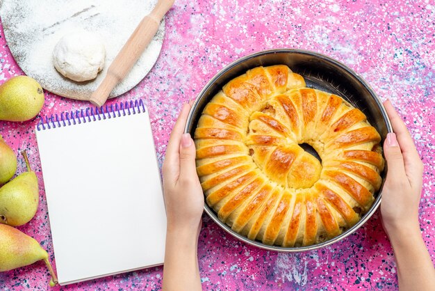 Vista superior del brazalete de pastelería horneada deliciosa formada dentro de una bandeja con masa de bloc de notas y peras en un escritorio brillante, pastelería galleta galleta azúcar dulce