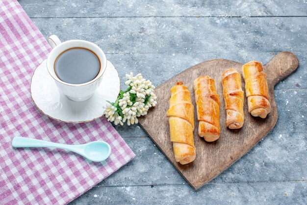 Vista superior brazaletes deliciosos dulces con relleno junto con una taza de café en la mesa de madera clara galleta de galleta de pastelería dulce de azúcar