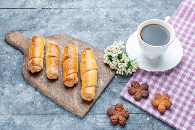 Vista superior brazaletes deliciosos dulces con relleno junto con una taza de galletas de café en la mesa de madera gris galleta de galleta de pastelería de azúcar dulce hornear