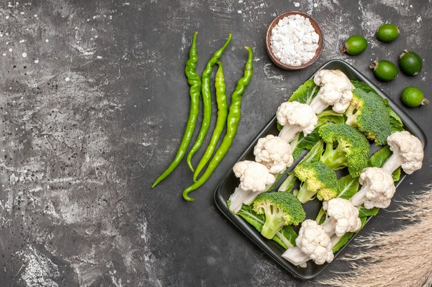 Vista superior de brócoli crudo y coliflor en un plato rectangular negro pimientos picantes verdes sal marina feykhoas en superficie oscura espacio libre comida foto