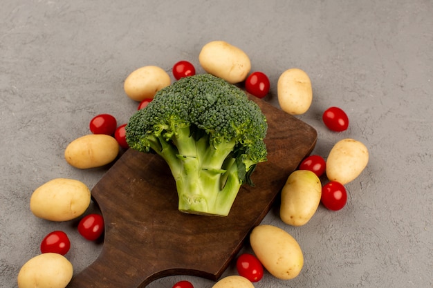 Vista superior de brócoli verde fresco junto con patatas tomates en el escritorio gris