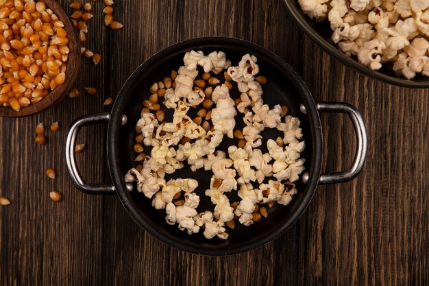 Vista superior de la cacerola con palomitas de maíz con granos de maíz en un cuenco de madera en una pared de madera