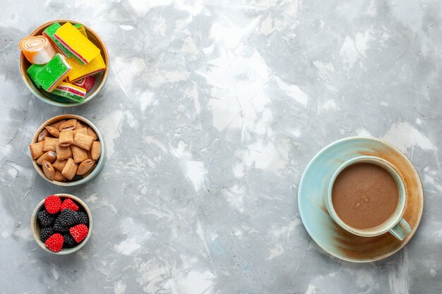 Vista superior de café con leche con galletas, confituras de bayas y dulces en el escritorio de luz.