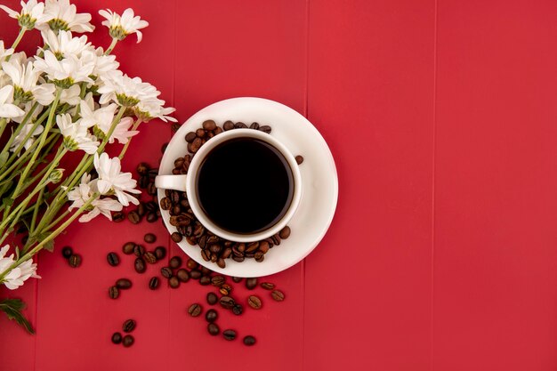 Vista superior de café en una taza blanca con flores sobre un fondo rojo con espacio de copia