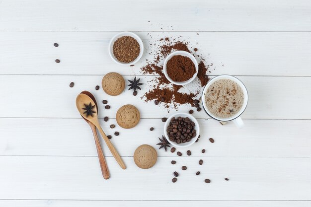 Vista superior de café en taza con granos de café, café molido, especias, galletas, cucharas de madera sobre fondo de madera. horizontal