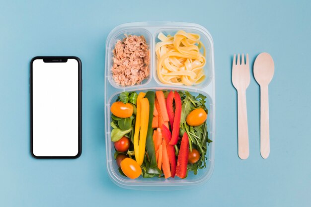 Vista superior caja de almuerzo de trabajo con teléfono en blanco