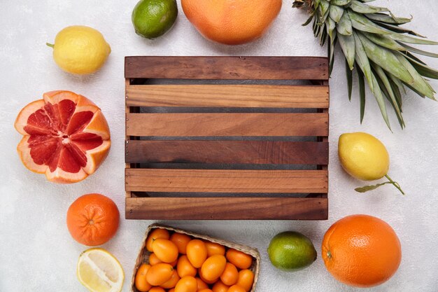 Vista superior de la caja con frutas cítricas como kumquats de naranja pomelo limón mandarina lima con hojas de piña sobre fondo blanco