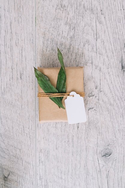 La vista superior de la caja de regalo envuelta marrón con la etiqueta y el verde se va en la tabla de madera