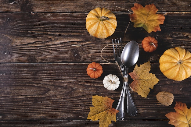 Vista superior de calabazas frescas, nueces, hojas de otoño con un tenedor y cuchara en una mesa de madera