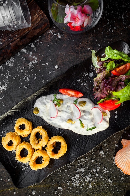 Vista superior de calamares rebozados con salsa y ensalada de verduras frescas en la bandeja