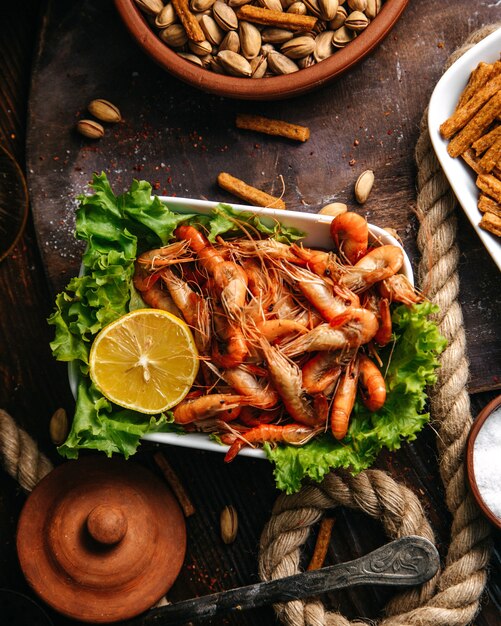 Una vista superior de camarones cocidos con ensalada verde y limón en la mesa de madera comida comida mariscos