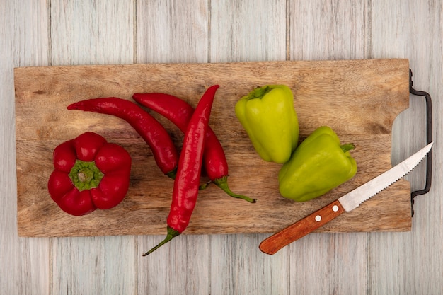 Foto gratuita vista superior de la campana de colores y chiles en una tabla de cocina de madera con un cuchillo sobre una superficie de madera gris