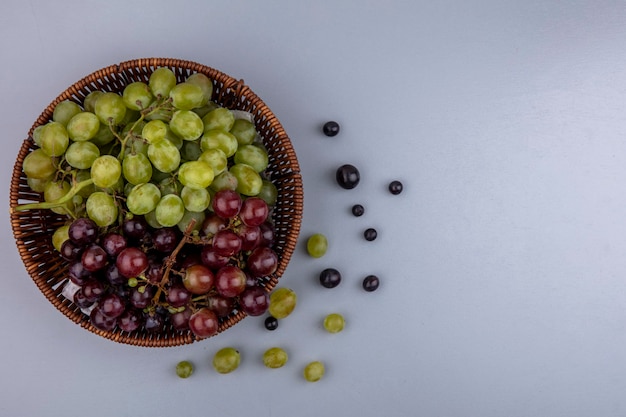 Vista superior de la canasta de uvas y bayas de uva sobre fondo gris con espacio de copia