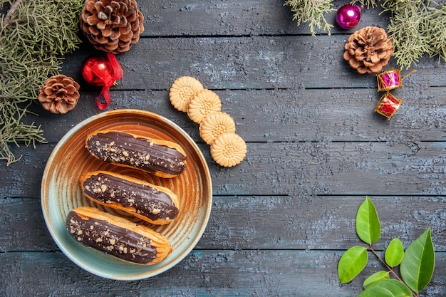 Foto gratuita vista superior canutillos de chocolate en una placa ovalada piñas juguetes de navidad hojas de abeto galletas y hojas sobre suelo de madera oscura con espacio de copia