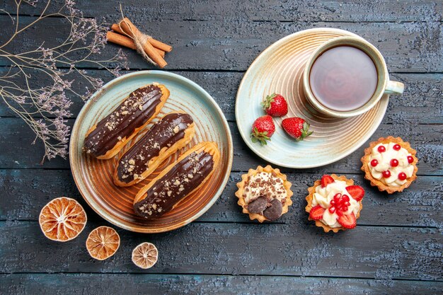 Vista superior canutillos de chocolate en placa ovalada una taza de té tartas de limones secos y canela sobre la mesa de madera oscura