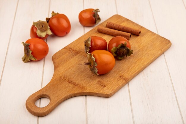 Vista superior de caquis suaves y jugosos en una tabla de cocina de madera con ramas de canela sobre una superficie de madera blanca