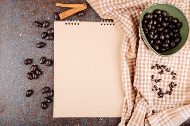 Vista superior de caramelo de nuez de chocolate glaseado en un tazón y cuaderno de bocetos sobre fondo negro