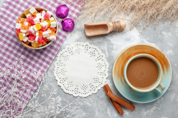 Vista superior de caramelos y canela junto con café con leche en la mesa de luz, bombones dulces de azúcar dulce