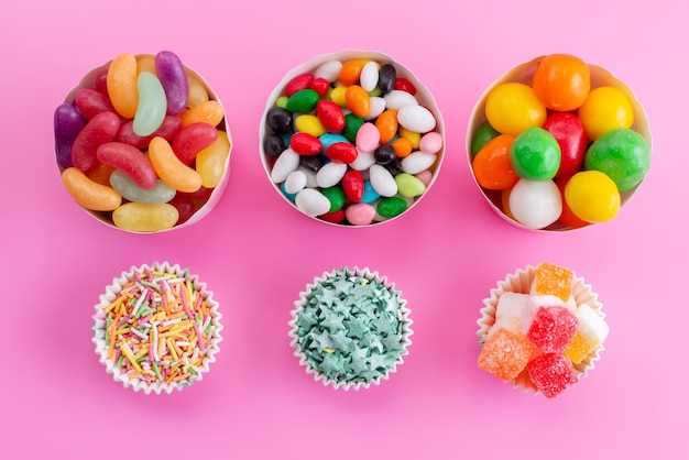Una vista superior de caramelos de colores dentro de diferentes paquetes de papel en el escritorio rosa