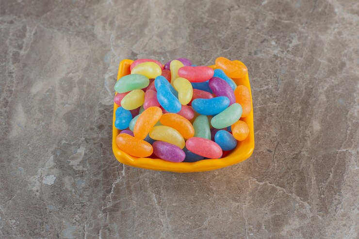 Foto gratuito vista superior de caramelos de colores en tazón de fuente naranja sobre superficie gris.