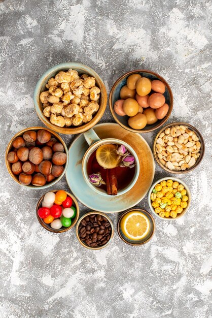 Vista superior de caramelos dulces con nueces y taza de té sobre superficie blanca