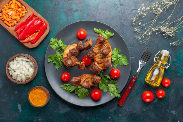 Vista superior de carne cocida en rodajas con aceite de tomates cherry verdes y condimentos sobre fondo azul.