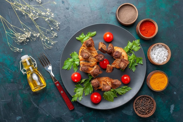 Vista superior de carne cocida en rodajas con aceite de tomates cherry verdes y condimentos sobre fondo azul.