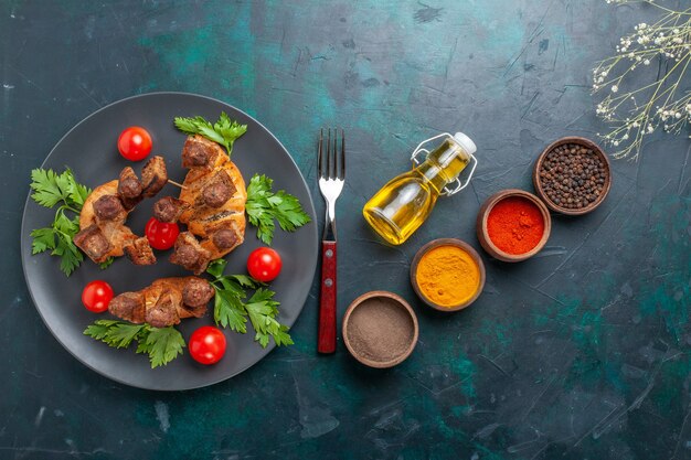 Vista superior de carne cocida en rodajas con tomates cherry y condimentos sobre fondo azul.