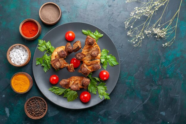 Vista superior de carne cocida en rodajas con tomates cherry verdes y condimentos en el escritorio azul