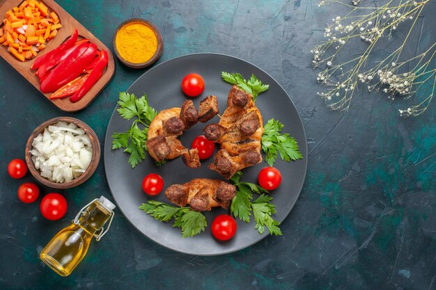 Vista superior de la carne cocida en rodajas con verdes tomates cherry y aceite de oliva sobre el fondo azul.