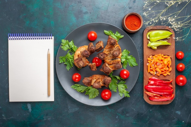 Vista superior de la carne cocida en rodajas con verduras y tomates cherry dentro de la placa en el escritorio azul