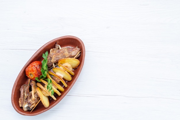 Vista superior de la carne frita con verduras y ciruelas al horno dentro de la placa marrón en el escritorio de luz, cena de plato de carne de comida