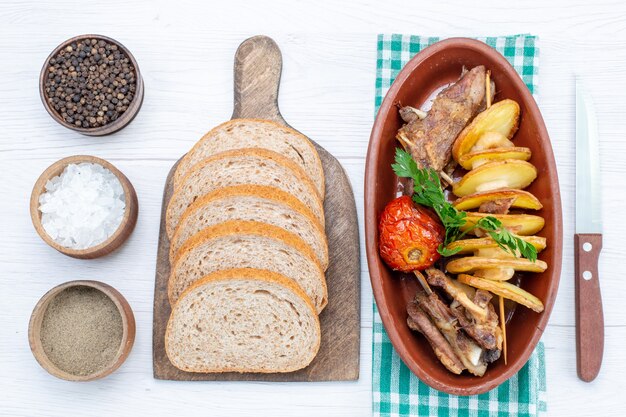 Vista superior de la carne frita con verduras y ciruelas al horno dentro de la placa con panes de pan sal en la mesa de luz, comida plato de carne cena vegetal