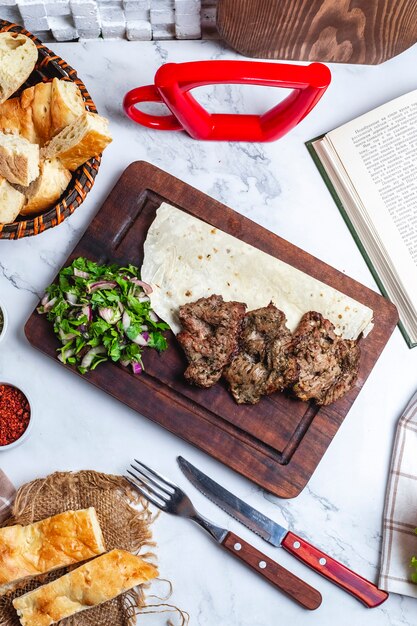 Vista superior de carne de kebab con especias y hierbas en lavash sobre una tabla de madera