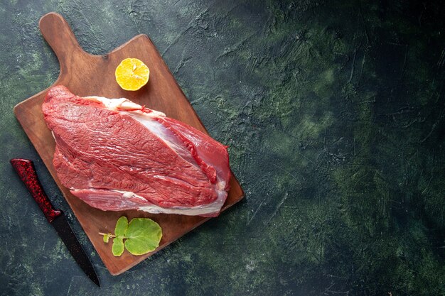 Vista superior de carnes rojas crudas frescas limón sobre tabla de cortar de madera marrón y cuchillo sobre fondo de color oscuro