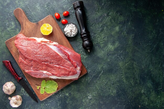 Vista superior de carnes rojas crudas frescas limón sobre tabla de cortar de madera marrón y verduras de cuchillo martillo de madera sobre fondo de color oscuro