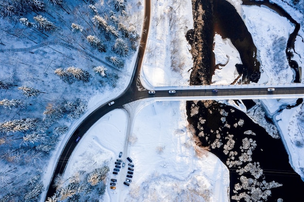 Vista superior de una carretera con curvas sobre un río que fluye a través del bosque cubierto de nieve