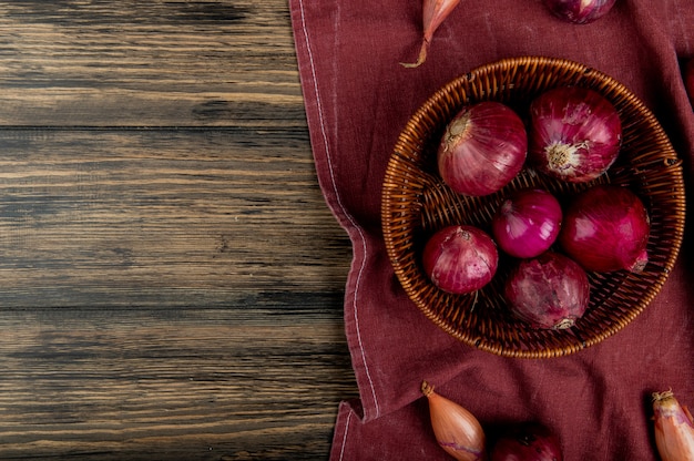 Foto gratuita vista superior de cebollas rojas en canasta con chalotes en tela bordo y fondo de madera con espacio de copia