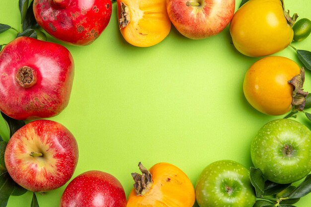 Vista superior de cerca coloridas frutas coloridas manzanas caquis Granada con hojas sobre la mesa