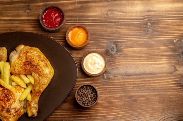 Foto gratuita vista superior de cerca coloridos cuencos de salsas de salsas de colores y pimienta negra junto al plato de pollo y papas fritas