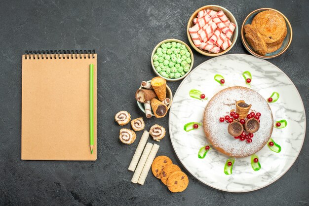 Vista superior de cerca dulces un pastel con grosellas rojas caramelos coloridos waffles cuaderno lápiz