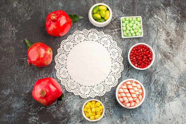 Vista superior de cerca dulces tazones de frutas cítricas de granada de caramelos coloridos alrededor de tapete de encaje