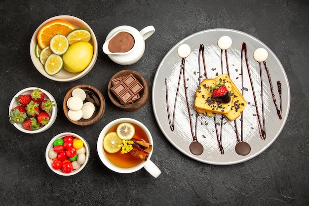 Vista superior de cerca dulces en tazones una taza de té con limón los tazones de frutas cítricas dulces de chocolate fresas crema de chocolate y el plato de pastel