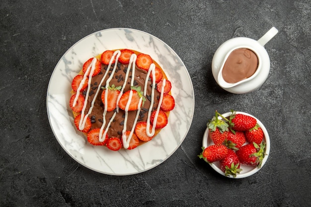 Vista superior de cerca fresas con crema de chocolate tazones de fresas y tarta de crema de chocolate con fresas y chocolate