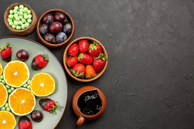 Vista superior de cerca frutas caramelos verdes fresa cubierta de chocolate naranja picada y tazones de bayas y salsa de chocolate sobre la mesa