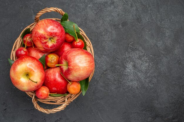 Vista superior de cerca frutas cerezas y manzanas en la canasta sobre la mesa oscura