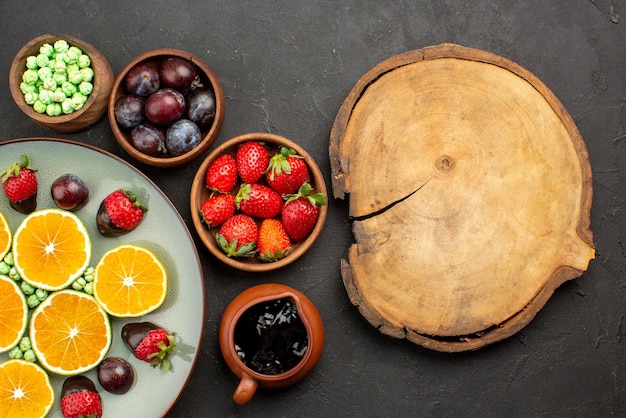 Vista superior de cerca frutas dulces verdes fresa cubierta de chocolate naranja picada y tazones de bayas y salsa de chocolate junto a la tabla de cocina de madera