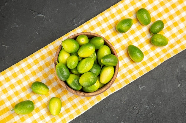 Foto gratuita vista superior de cerca frutas frutas en un tazón sobre el mantel blanco-amarillo sobre la mesa oscura